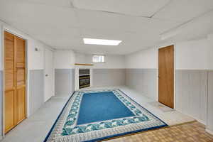 Interior space featuring visible vents, wainscoting, a glass covered fireplace, a drop ceiling, and light floors