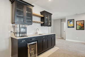 Kitchen featuring tasteful backsplash, light colored carpet, light stone counters, a sink, and beverage cooler