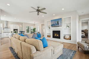 Living area with built in features, ceiling fan, light wood-style flooring, a glass covered fireplace, and recessed lighting