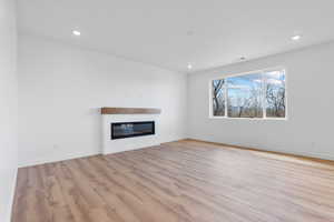 Unfurnished living room with recessed lighting, light wood-style floors, a glass covered fireplace, and baseboards