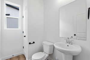 Half bath with baseboards, toilet, wood finished floors, and a sink