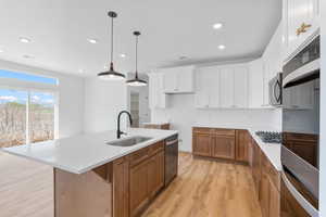 Kitchen featuring a sink, brown cabinetry, a kitchen island with sink, stainless steel appliances, and light wood finished floors