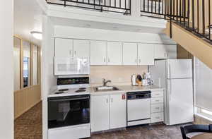 Kitchen featuring white cabinets, a sink, light countertops, white appliances, and a towering ceiling
