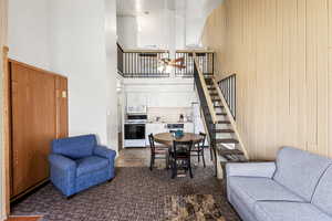 Living room with ceiling fan, a towering ceiling, wooden walls, and stairway