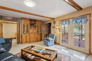 Living room featuring baseboards, a wood stove, beam ceiling, french doors, and light carpet