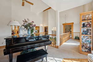Living area featuring ceiling fan with notable chandelier, a towering ceiling, carpet, and an upstairs landing