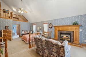 Bedroom with a fireplace, lofted ceiling, light carpet, and wallpapered walls