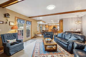 Living room featuring a chandelier, light colored carpet, beamed ceiling, and baseboards