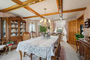 Dining area featuring an inviting chandelier, light colored carpet, coffered ceiling, wallpapered walls, and beam ceiling