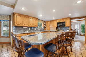 Kitchen with a sink, light tile patterned floors, black microwave, and decorative backsplash