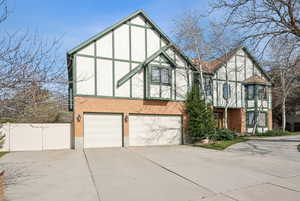 English style home with a garage, stucco siding, fence, brick siding, and driveway