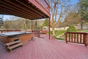 Deck with a covered hot tub, a fenced backyard, and a lawn