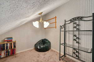 Interior space featuring a chandelier, carpet, a textured ceiling, and vaulted ceiling