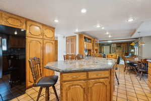 Kitchen with light tile patterned floors, a kitchen breakfast bar, a textured ceiling, and a kitchen island