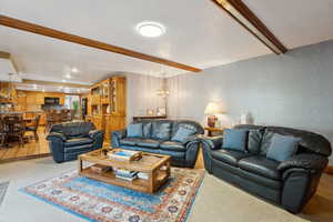 Living room featuring wallpapered walls, a chandelier, a textured ceiling, carpet floors, and beam ceiling