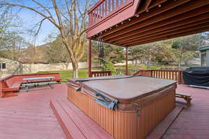 Wooden deck featuring a lawn, a covered hot tub, fence, and area for grilling