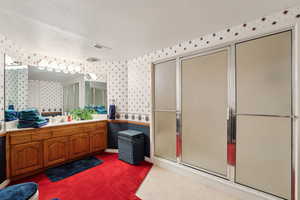 Full bath with visible vents, a textured ceiling, vanity, wallpapered walls, and a shower with door