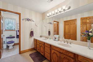 Full bath featuring a sink, wallpapered walls, double vanity, and a textured ceiling
