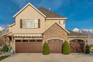 View of front facade featuring roof with shingles, concrete driveway, stucco siding, and stone siding