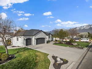 View of front of property featuring a garage, a front yard, stone siding, a mountain view, and driveway