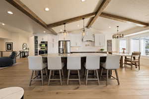 Kitchen featuring white cabinets, a breakfast bar, premium range hood, lofted ceiling with beams, and appliances with stainless steel finishes