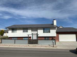 Raised ranch featuring an attached garage, fence, driveway, and a chimney