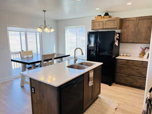 Kitchen with a notable chandelier, a sink, light countertops, light wood-style floors, and black appliances