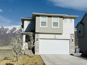 View of front of property featuring concrete driveway, stone siding, a mountain view, and an attached garage