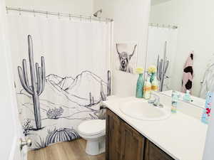 Full bathroom with toilet, curtained shower, vanity, and wood finished floors