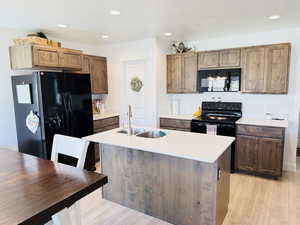 Kitchen featuring a sink, light countertops, black appliances, and light wood-style floors