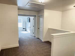 Corridor with a textured ceiling, attic access, an upstairs landing, dark colored carpet, and baseboards