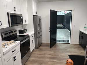 Basement Kitchen featuring appliances with stainless steel finishes, light wood finished floors, light countertops, and white cabinetry