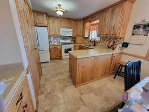 Kitchen featuring white appliances, a peninsula, light countertops, backsplash, and a sink