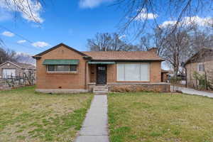 Bungalow with a front yard, fence, brick siding, and a chimney