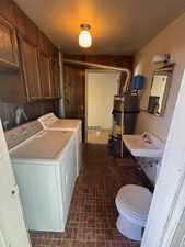 Laundry room featuring brick patterned floor, visible vents, water heater, a sink, and washer and clothes dryer