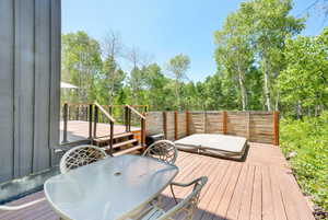 Wooden terrace featuring outdoor dining space and view of wooded area
