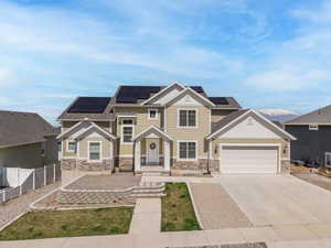 Craftsman-style home with roof mounted solar panels, driveway, stone siding, and fence