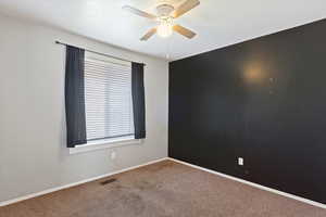 Carpeted spare room with visible vents, baseboards, and a ceiling fan