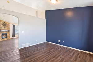 Empty room with baseboards, a fireplace, visible vents, arched walkways, and wood finished floors
