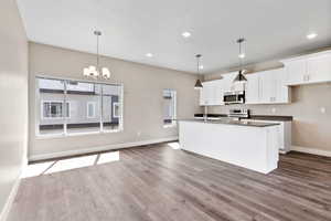 Kitchen with a notable chandelier, dark wood-style flooring, baseboards, recessed lighting, and stainless steel appliances