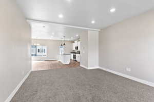 Unfurnished living room with baseboards, a sink, a chandelier, carpet floors, and recessed lighting