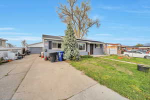 Ranch-style house featuring a front yard, a detached garage, fence, and roof mounted solar panels. Extra long cement driveway.