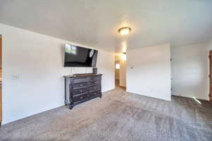 Unfurnished living room featuring a textured ceiling, carpet flooring, and baseboards