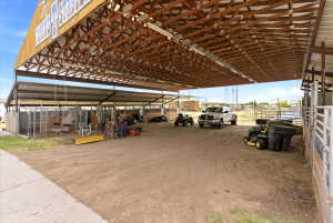 Spacious covered outdoor structure featuring a metal roof with exposed wood trusses, concrete flooring, and metal fencing