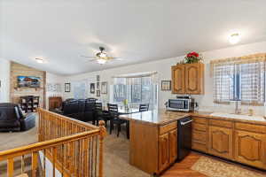 Open-concept kitchen featuring wood cabinetry, a built-in dishwasher, and a stone-finish countertop