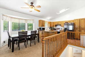Open-concept kitchen and dining area featuring warm wood cabinetry, a central island with countertop seating, and a bay window
