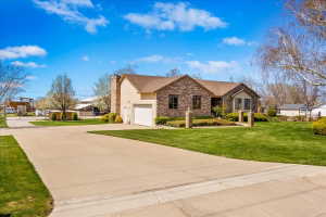 Ranch-style residence featuring a brick facade and light-colored siding, an attached garage with a white door, and a prominent brick chimney