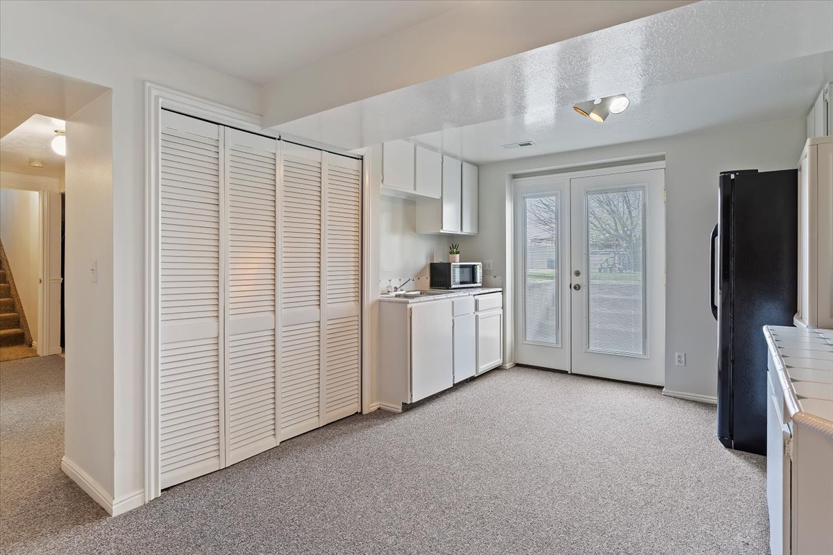 Carpeted room featuring louvered bi-fold closet doors, white cabinetry, a single-basin sink, and double glass-paneled patio doors