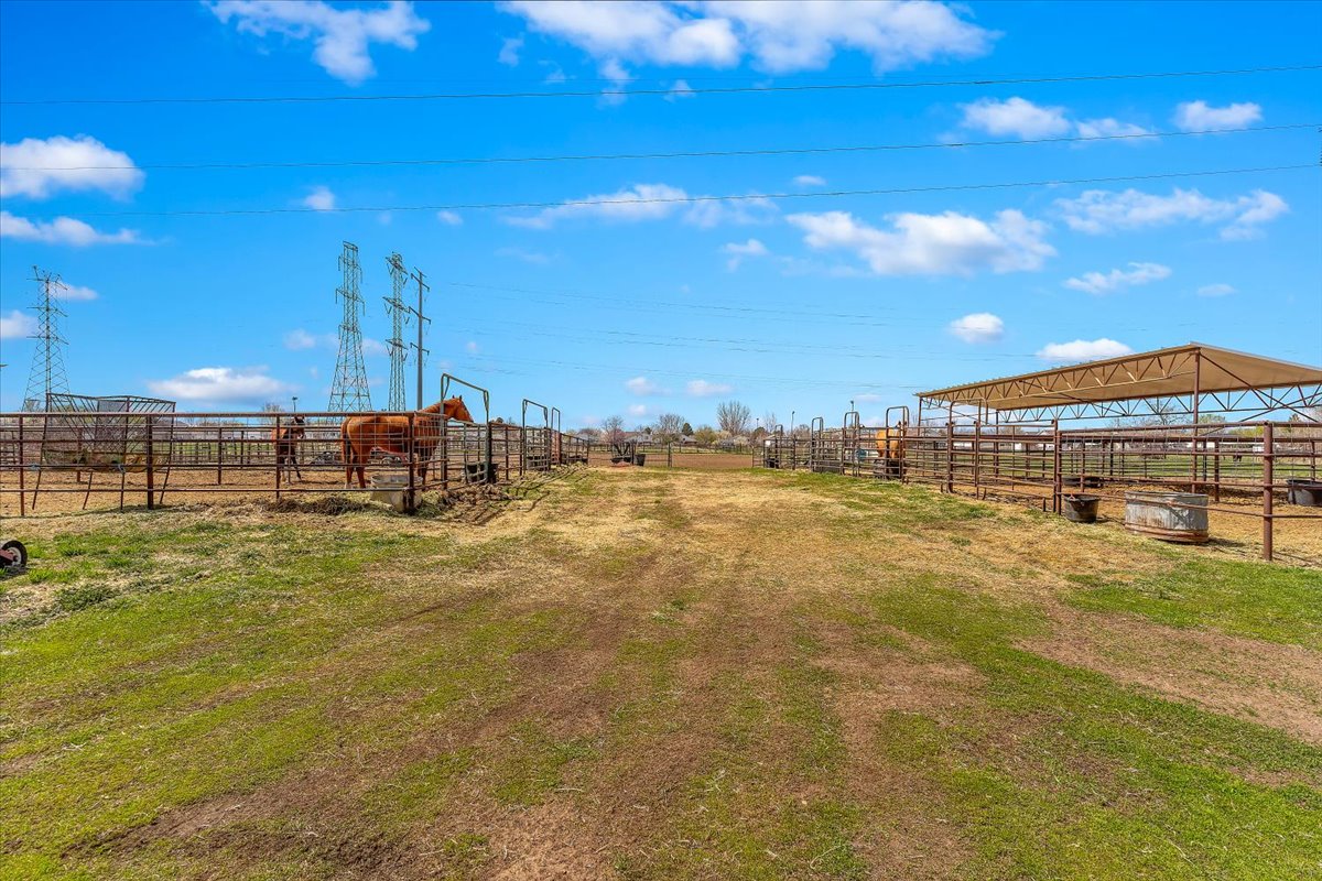 Expansive outdoor property featuring fenced enclosures, an open-air covered structure, a clear pathway, and visible power lines in the distance
