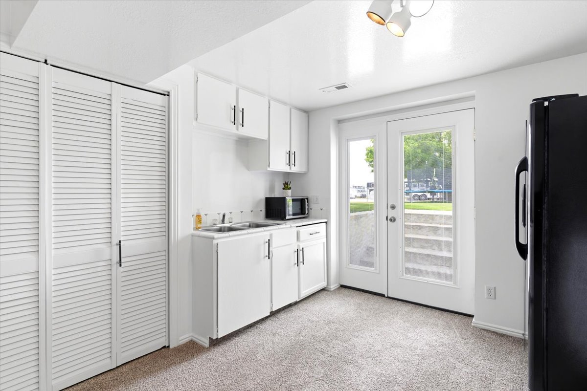 Compact kitchen space featuring white cabinetry, a double basin sink, and a black refrigerator